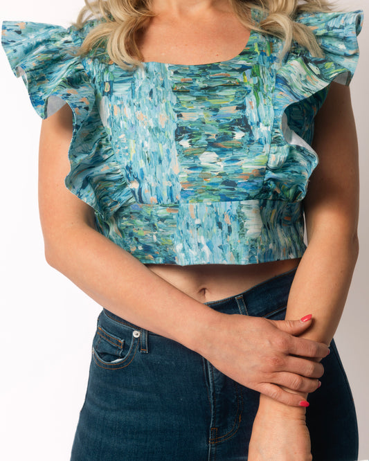 Woman wearing a blue and green patterned top with ruffled sleeves on a plain background