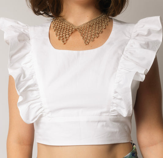 White top with ruffled sleeves and a gold bib necklace on a neutral background