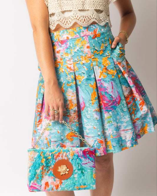 Person wearing a colorful floral skirt with a matching clutch on a plain background