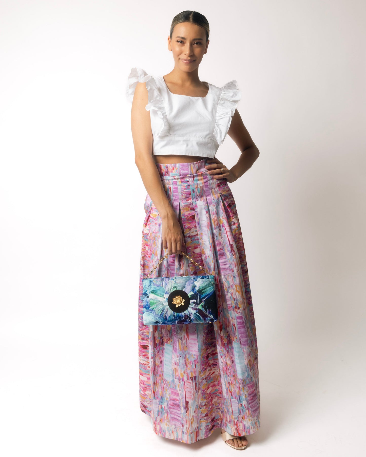 Woman wearing a pink colorful skirt holding a patterned clutch against a white background