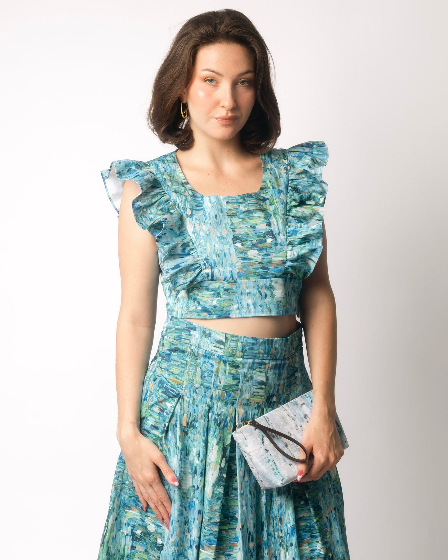 Woman wearing a blue floral dress holding a clutch against a white background