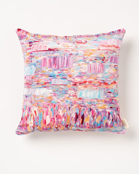 A square-shaped throw pillow with a multicolored geometric pattern in shades of pink, blue, and white.