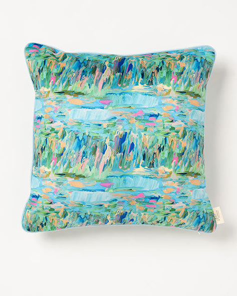 A square-shaped throw pillow with a multicolored design featuring shades of blue and green, and baby blue cording along the edges.