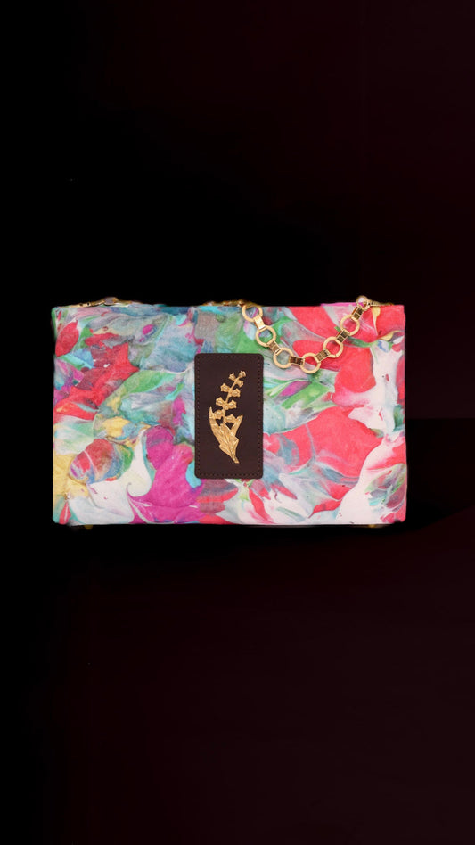Multicolored floral-patterned clutch bag with a gold chain on a black background